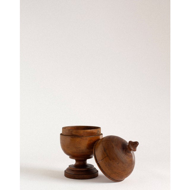 A turned apothecary jar crafted from solid walnut wood, shaped with a rounded body and a softly domed lid finished with a...