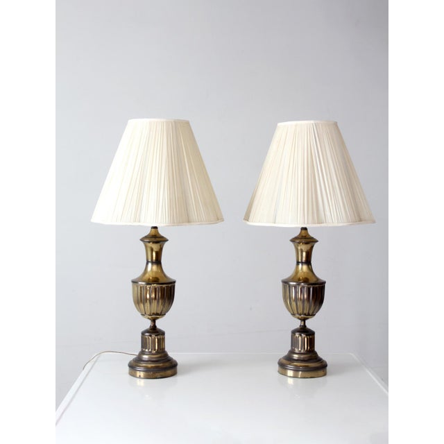 A pair of vintage 1970s brass table lamps in a refined Neoclassical urn form. Fluted bodies, stepped bases, and tall,...