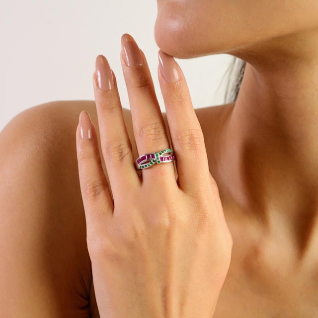 Elegant infinity band ring crafted in 925 sterling silver, featuring square-cut emeralds paired with round ruby accents in...
