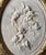A striking neoclassical carved marble bas-relief depicting three cherubs in high relief, presented in an ornate oval gilt...