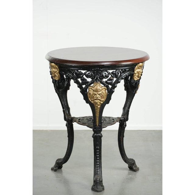 An antique English bistro/side table with a cast-iron base dates from the early 20th century and features a solid wood...