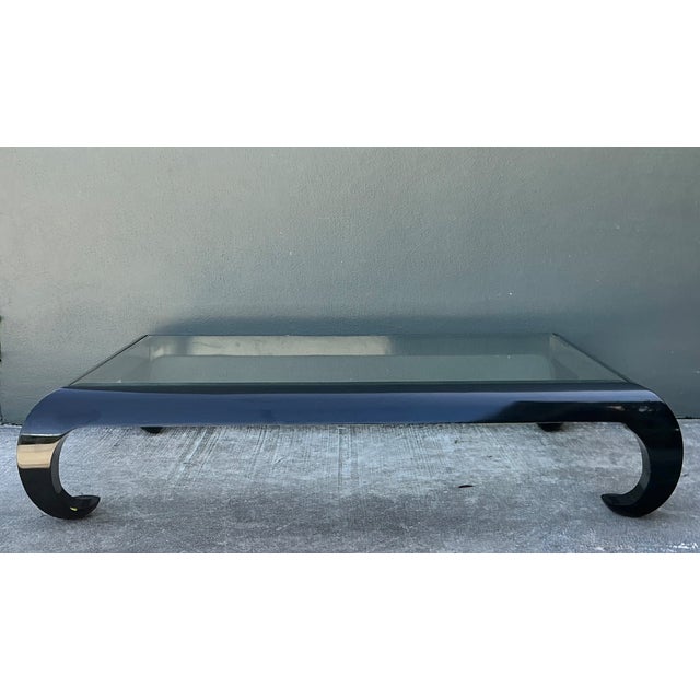 This vintage coffee table pairs a glossy black lacquered wood frame with a clear glass top, a modernist combination that...