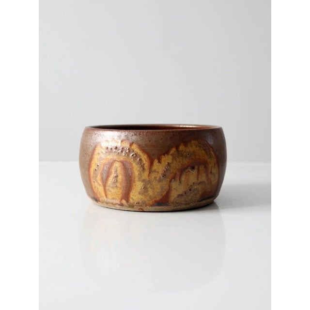 A vintage studio pottery bowl signed by the artist, featuring a warm brown glaze complemented by goldenrod accents. The...