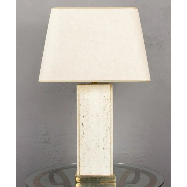 A striking French Mid-Century table lamp from the 1960s, featuring a substantial rectangular travertine body raised on a...