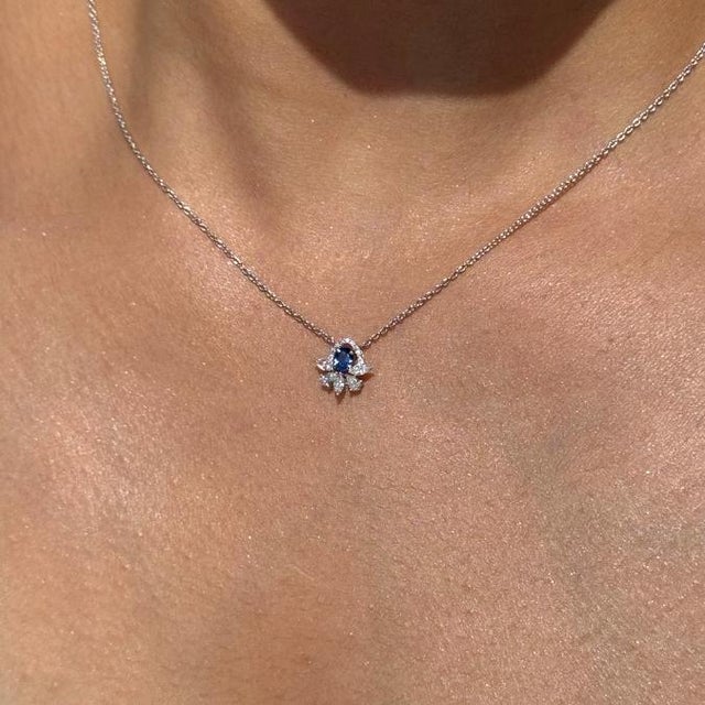 This floral pendant necklace features a 0.24 carat blue sapphire set in 14K white gold, measuring approximately 3.2 x 4.2...