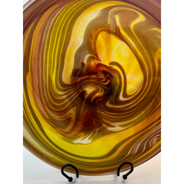 Hand blown art glass charger with swirling design of yellow, green and salmon. Can be used as a a bowl or displayed on...