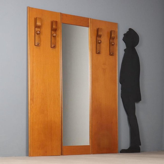 1960s-70s entryway furniture featuring a wooden structure with a practical central mirror and side coat racks. The linear...
