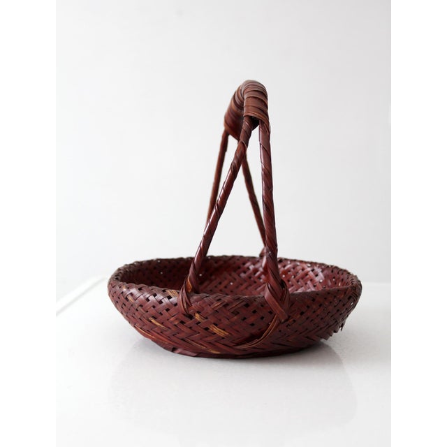 Vintage hand-woven bamboo basket featuring a wrapped handle and rich natural patina. Crafted with intricate woven detail...