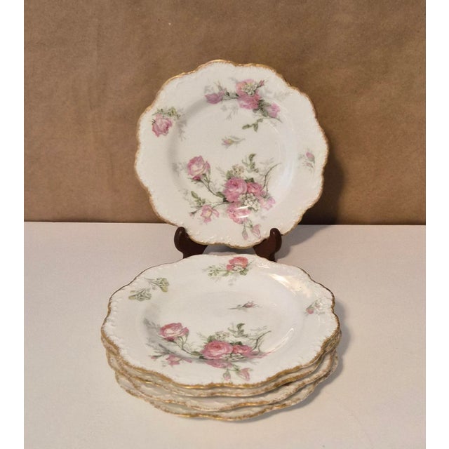 Elegant hand-painted Limoges porcelain plates featuring delicate pink roses and green foliage accented by a refined gold...