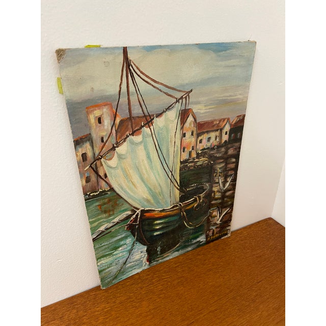 This vintage painting on canvas board depicts a harbor scene featuring a single-mast sailboat docked along a stone quay,...