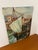 This vintage painting on canvas board depicts a harbor scene featuring a single-mast sailboat docked along a stone quay,...