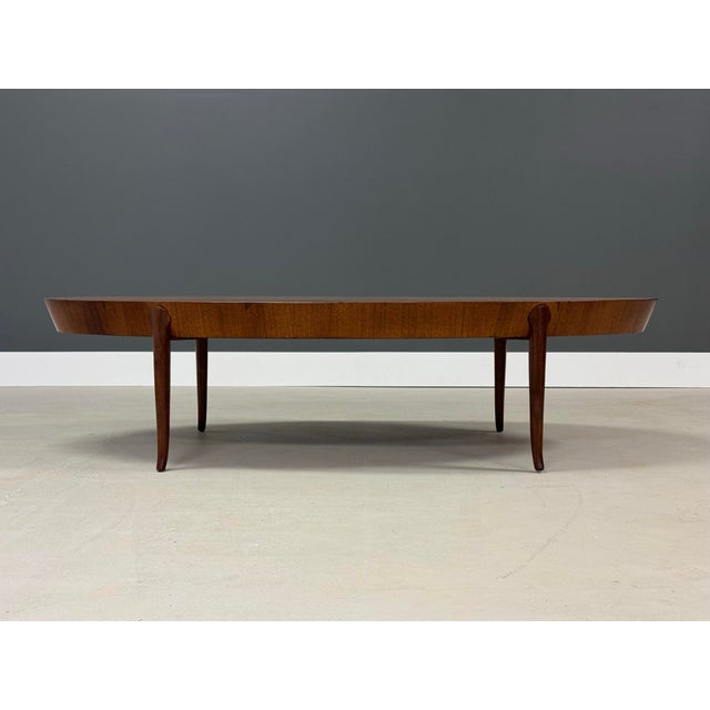 A mid century modern walnut oval coffee table designed by T.H. Robsjohn Gibbings for Widdicomb with flared tip legs and...