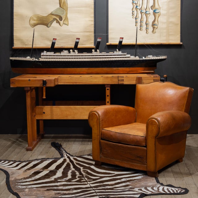 ABOUT Early 20th c. leather club chair with charming mustache top, riveted back, wooden feet, brown piping and rounded...