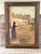 Large vintage oil on canvas depicting an elegant woman in period dress along a quiet European street. The architectural...