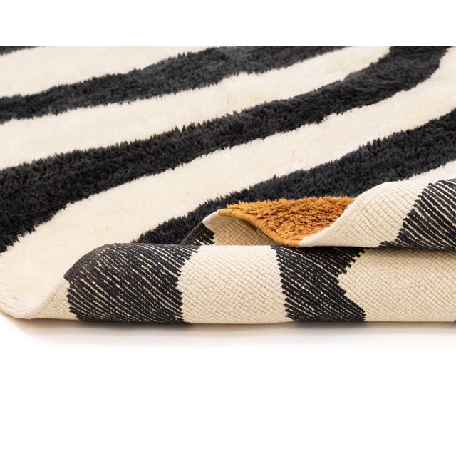 Abstract hand-knotted wool rug displaying Charcoal Black and Ivory zebra stripes with a central Gold Ochre swath that...