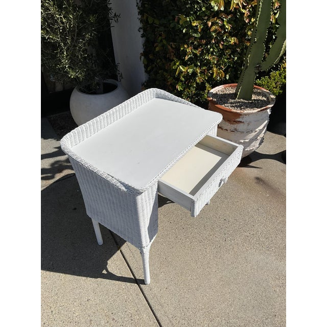 Vintage white wicker writing desk with single drawer and raised back detail. Features woven wicker construction over a...