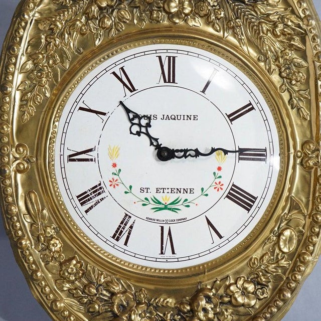 An antique French wag-on-the-wall clock offers brass construction with floral and foliate embossed frame, face with Roman...