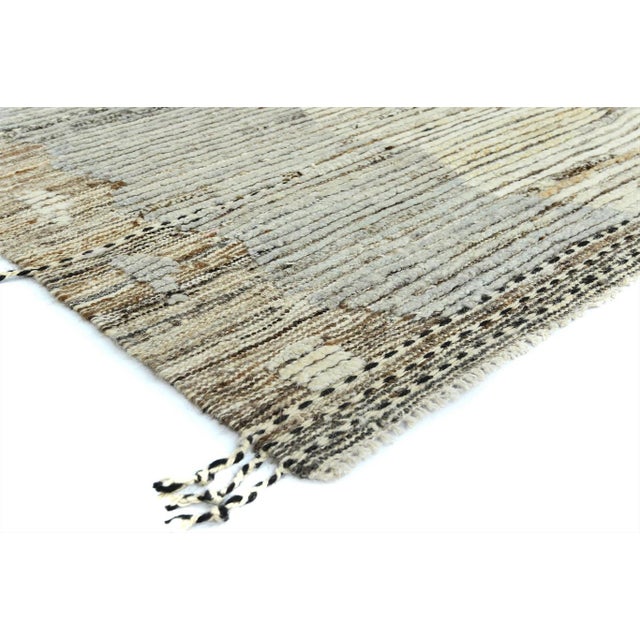 This contemporary Moroccan-style wool rug has a light gray, ivory, and light brown field with a tribal design. This rug...