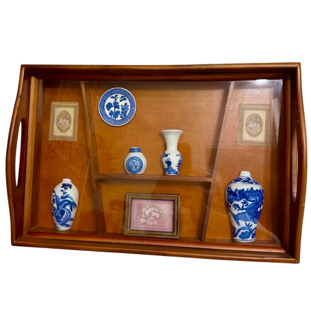 This decorative wooden display tray with compartments contains a collection of miniature blue and white porcelain items....