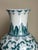 This tall porcelain vase features a classic Chinese-inspired floral and vine motif in green and blue over a bright white...