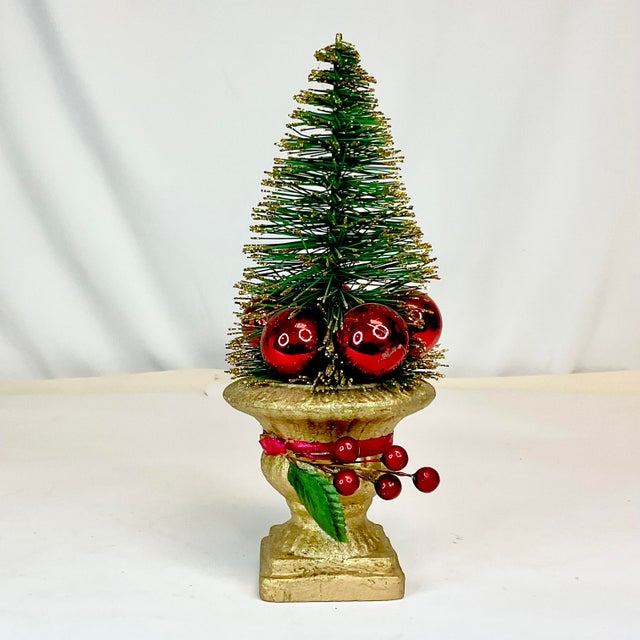 This is a pretty Bottle Brush Christmas Tree. It sits in a gold ceramic urn and is surrounded by red Christmas ornaments....