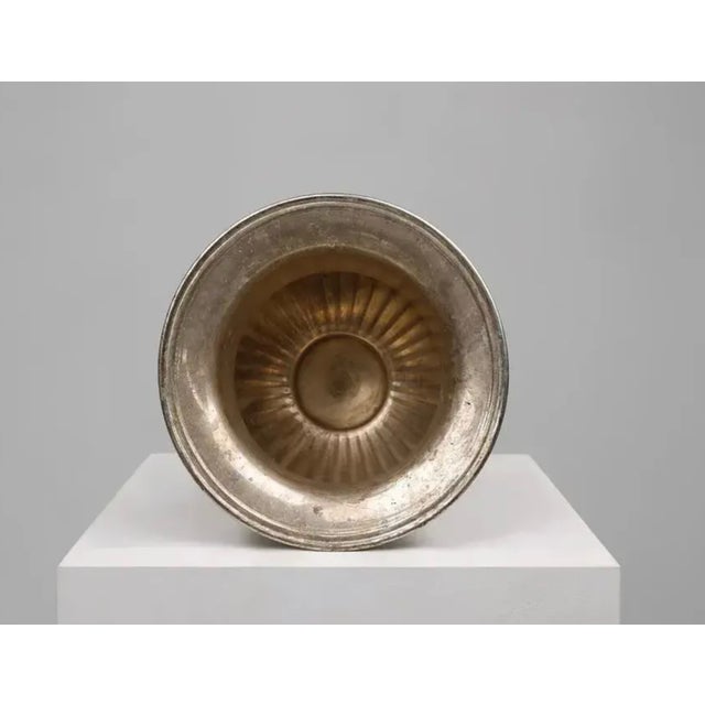 Elegant vintage silver-tone metal urn featuring a flared rim, pedestal base, and ornate decorative side handles. This...