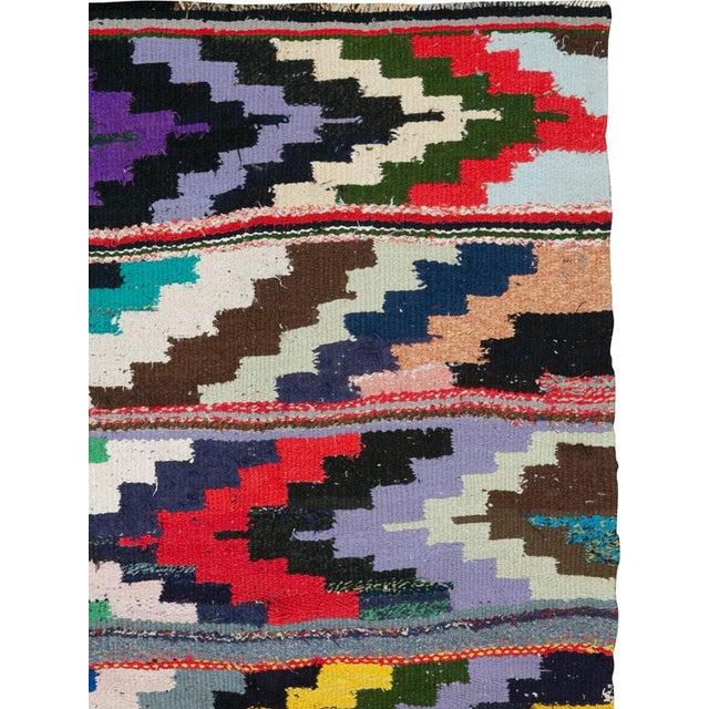 This Mid-20th century Persian flatweave kilim presents a bold, kinetic composition defined by sweeping, jagged bands that...