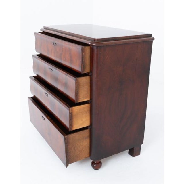 An elegant Biedermeier mahogany chest of drawers of rounded-corner form, raised upon turned feet The chest features a...