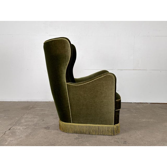 A Scandinavian mid-century wingback lounge chair, 1940s–1950s, in deep forest green velvet. A generous, fully upholstered...