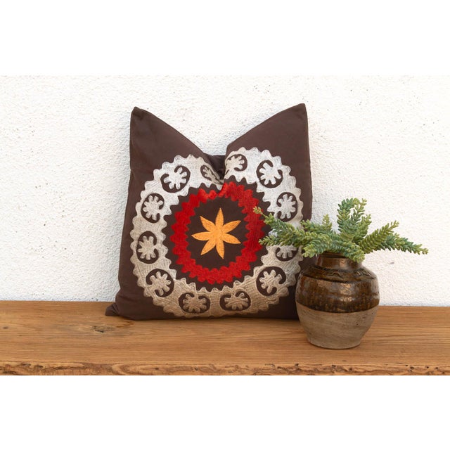A radiant orange-gold starburst sits at the center of this pillow, ringed first in red and then framed by a wide border of...