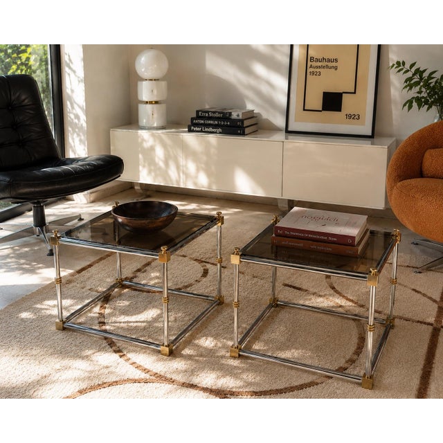 A sophisticated pair of vintage chrome, brass, and smoked glass side tables by Maison Jansen. Their restrained...