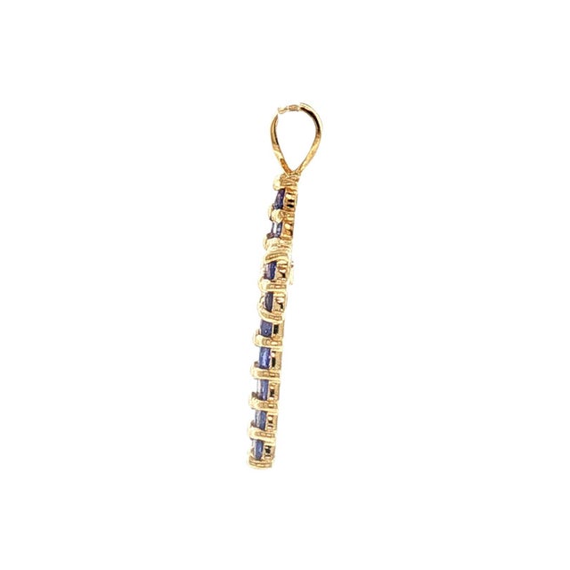 A late 20th-century 14k gold cross pendant featuring 26 round-cut natural tanzanite gemstones. The stones are a striking...