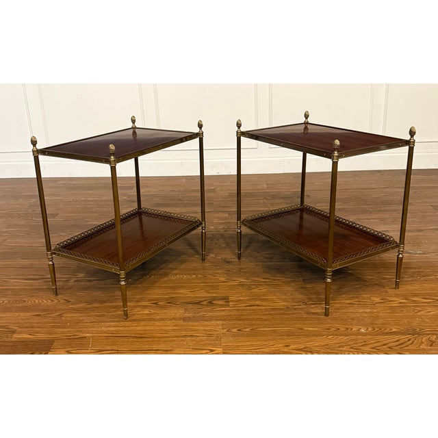 This is a pair of classic two-tiered wood and brass end tables by Leighton Hall Furniture. The top and bottom shelves are...