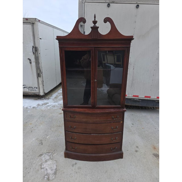 Classic vintage china cabinet featuring an elegant curved (bow-front) silhouette with glass-paneled doors and ample...