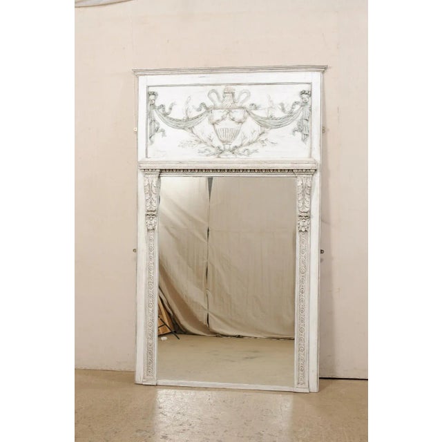 A French Neoclassic-style painted wood trumeau mirror. This vintage mirror from France features the carved-wood plaque...