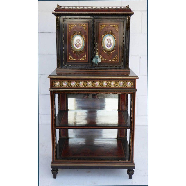 A 19th century amboyna and ebony cabinet, with three quarter balustrade gallery, above two panelled doors set with Paris...