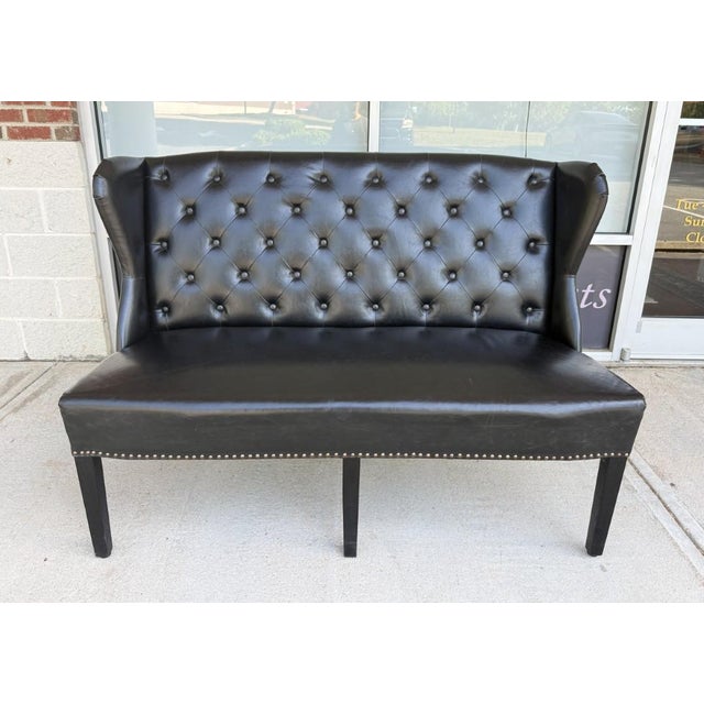 This Arhaus black tufted leather settee features a classic design with deep button tufting, wingback sides, and elegant...