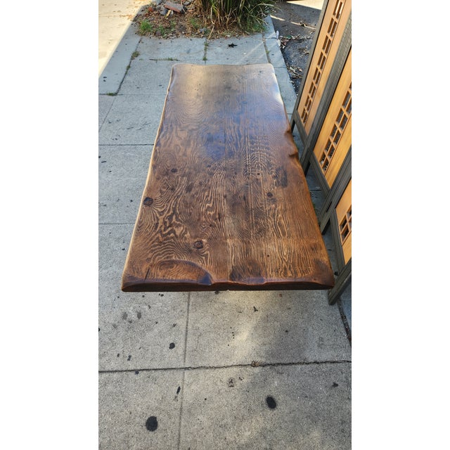 Rustic coffee table is constructed from a thick, solid wood slab with a live edge. The wood has a dark brown stained...