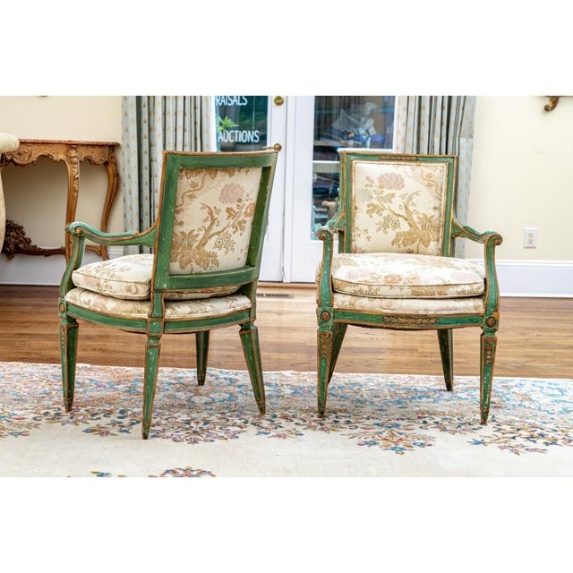 A very fine pair of antique armchairs with classic Louis XVI form. The frames are painted teal-green with parcel gilt...