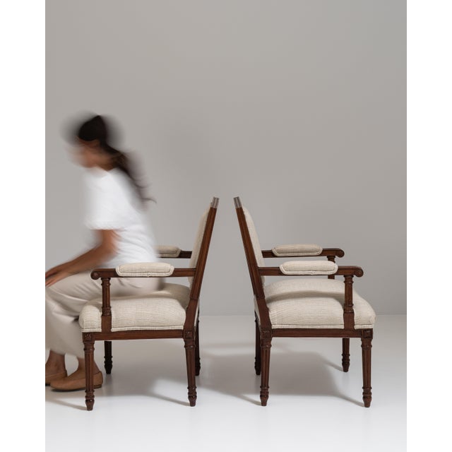 This pair of 19th century Louis XVI oak upholstered armchairs from France, made in dark oak with scrolled arms and cream...