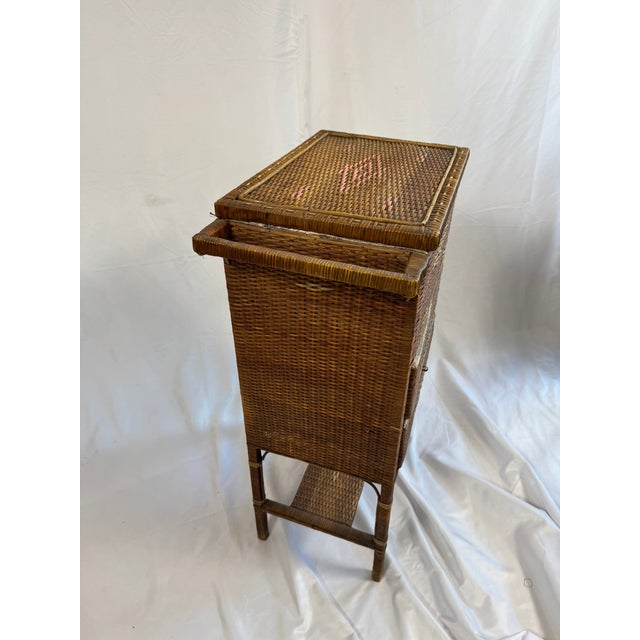 This is an antique woven rattan sewing stand, a tall, narrow work table with a hinged lift-lid top compartment and two...