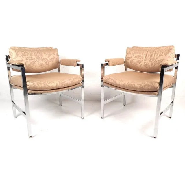 This elegant pair of chrome frame arm chairs features comfortable upholstered armrests with unique designs on the fabric....
