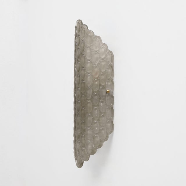 Elegant pair of wall sconces featuring large diffusers in soft smoked Murano glass, handcrafted with a refined relief...
