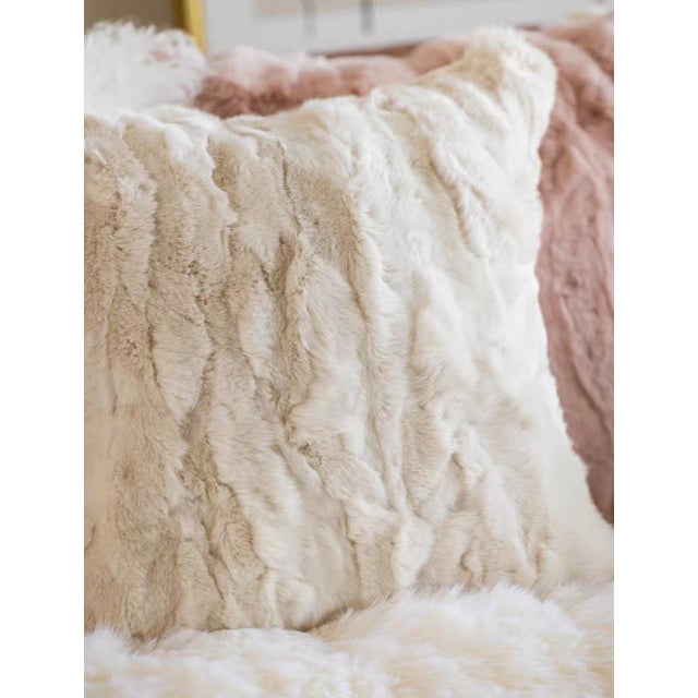 The fluffy, creamy white faux rabbit fur throw pillow, adorned in a languid and draped manner on the deep brown leather...