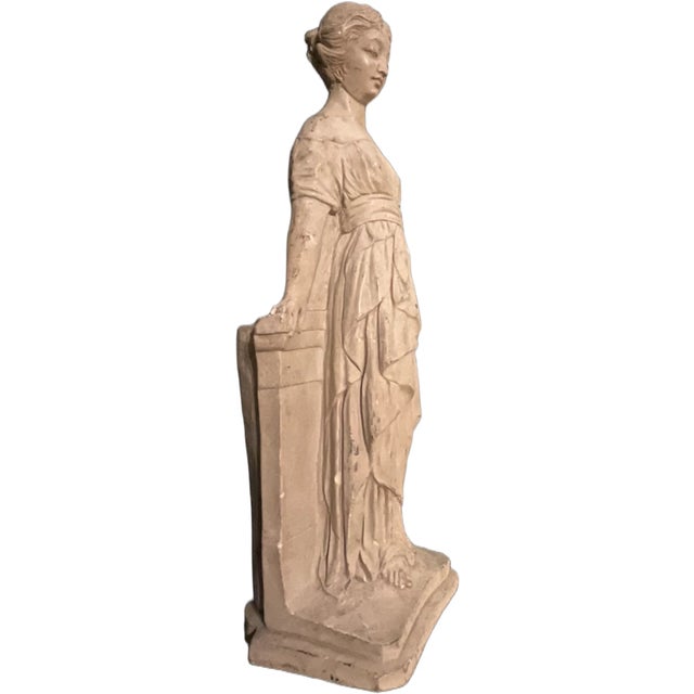 This graceful statue depicts a lady in a classic Empire waist gown, leaning elegantly against a pedestal. With its...