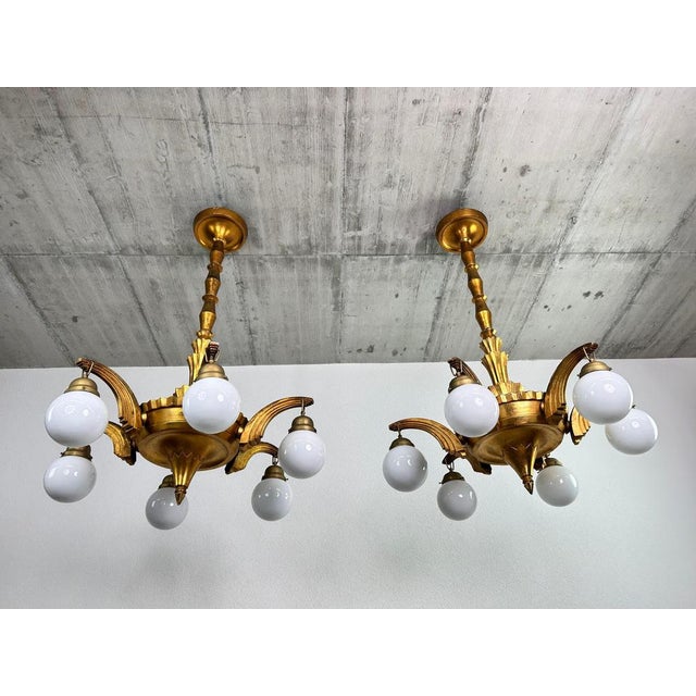 Large Art Deco wooden chandeliers in the style of Dagobert Peche, featuring elegant white opaline glass lampshades. The...