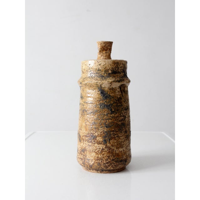 1970s handmade studio pottery jar featuring a tall cylindrical form, sculptural lid, and richly variegated earth-tone...