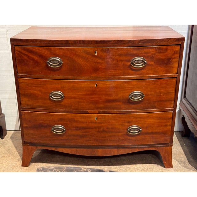 19th century mahogany bowfront chest with a crossbanded top over three long dovetailed drawers, each fitted with oval...