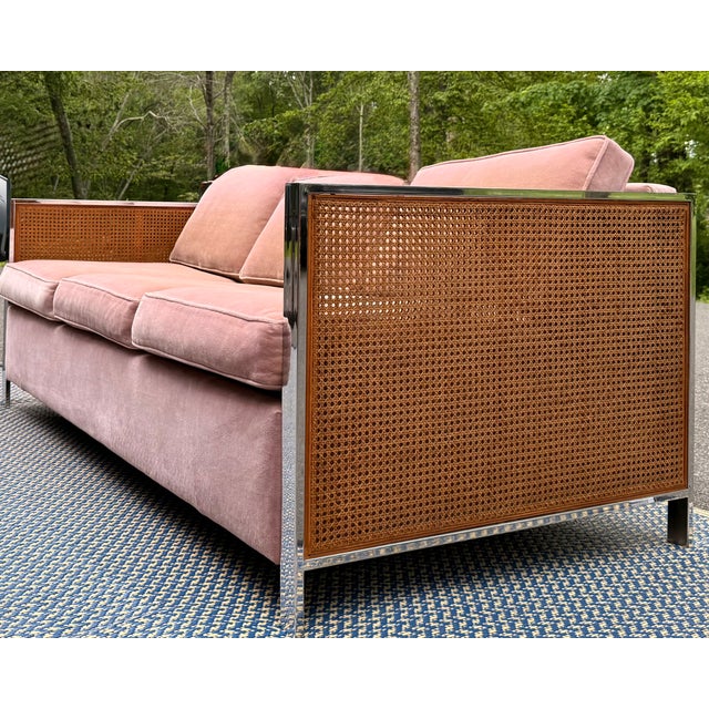 A striking vintage sleeper sofa featuring a polished chrome frame, woven cane side panels, and blush velvet upholstery....