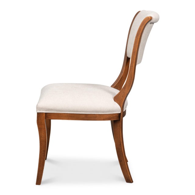 Swept saber legs and a curved crest rail follow the ancient Greek seating form, wrapping gently around the shoulders. The...